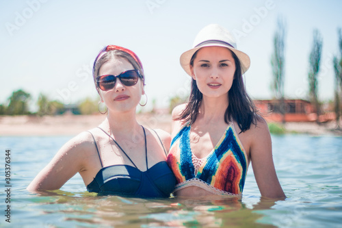 Two young tanned woman in crochet swimsuit and white hat swimming in sea.