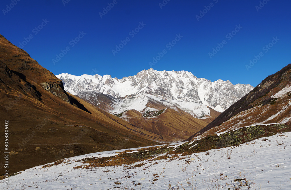 Fototapeta premium Mountain landscape panorama. Majestic mountain peaks covered with snow against a bright blue sky.