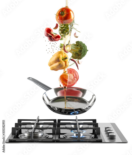 Black Glass gas cooking plate and chrome frying pan with flying colorful fresh vegetables and olive oil. Tomato, pepper, garlic and spices. White isolated background.