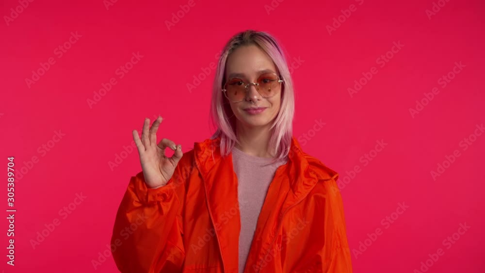 Young hipster making OK sign over pink background. Winner. Success. Positive girl smiles to camera. Body language. Young hipster making OK sign over pink background. Winner. Success. Positive girl smiles to camera. Body language.