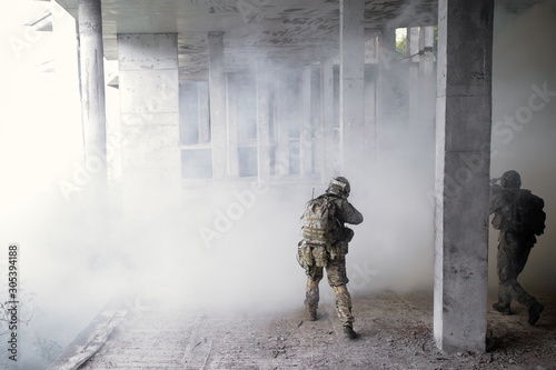 Fotografija Two military soldiers storming a destroyed building with terrorists in a smoke f