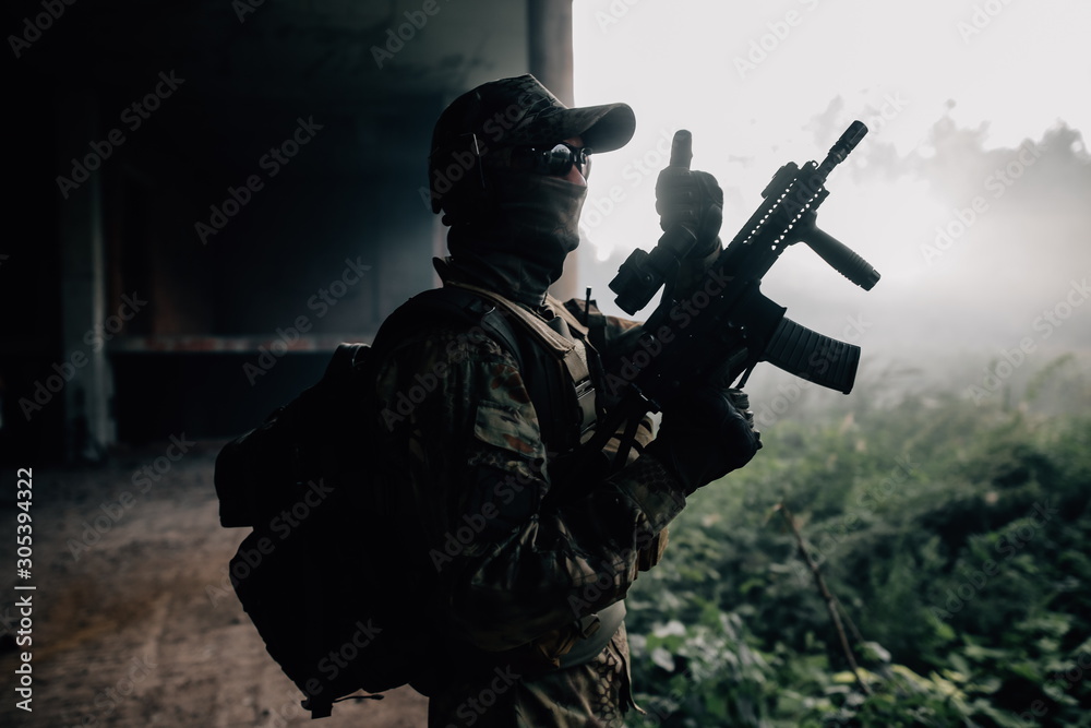 Army soldier in camouflage standing with assault rifle in hand among the stone jungle showing class. Military in the forests of the jungle