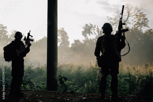 Two military soldier in camouflage with assault rifles standing in the forests of the jungle. Two terrorists standing in a rainforest
