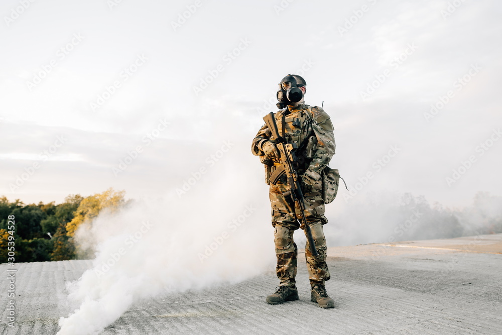 Military soldier in the smoke curtain with an assault rifle standing on the roof in a gas mask preparing for the assault. Wartime Military soldier in the smoke curtain with an assault rifle standing on the roof in a gas mask preparing for the assault. Wartime
