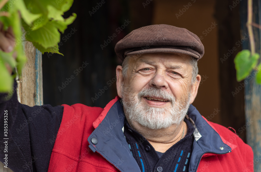 Nice positive portrait of Ukrainian bearded smiling senior peasant against old barn entry .