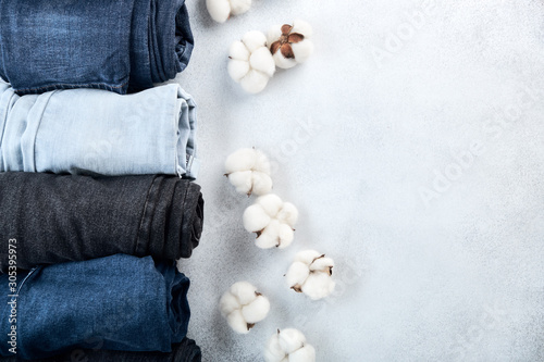 Row of rolled jeans and cotton flowers on light background