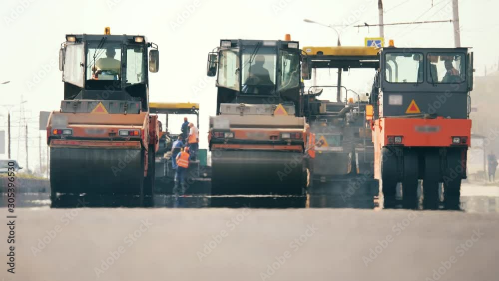 Front view of asphalt-placing machines and workers. Road construction process. Front view of asphalt-placing machines and workers. Road construction process.
