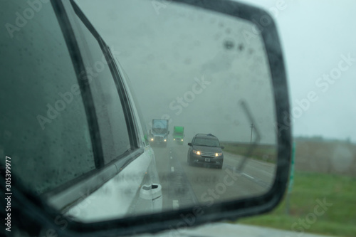 Vehicles on a highway are reflected in a car mirror during a rain in the US countrside © Rawf8