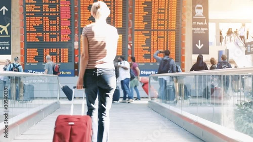 Woman checking departure time and boarding gate on flight information display board at international airport terminal travelling with suitcase, footage