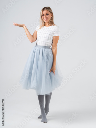 Full growth in profile blonde model girl standing barefoot in skirt gesture holds out her hand with a place for text. Copy space mockup. Idea for banner with women. Pastel colors white background