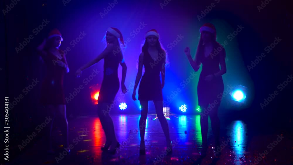 Girls in dresses and hats snow maidens dance in a nightclub. Smoky colorful background Girls in dresses and hats snow maidens dance in a nightclub. Smoky colorful background
