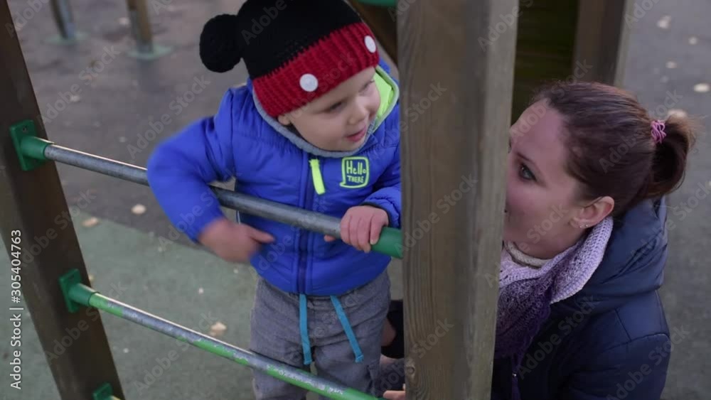 Mom plays with her son on the playground. Mother helps a 2-year-old boy climb the ladder. Mom plays with her son on the playground. Mother helps a 2-year-old boy climb the ladder.