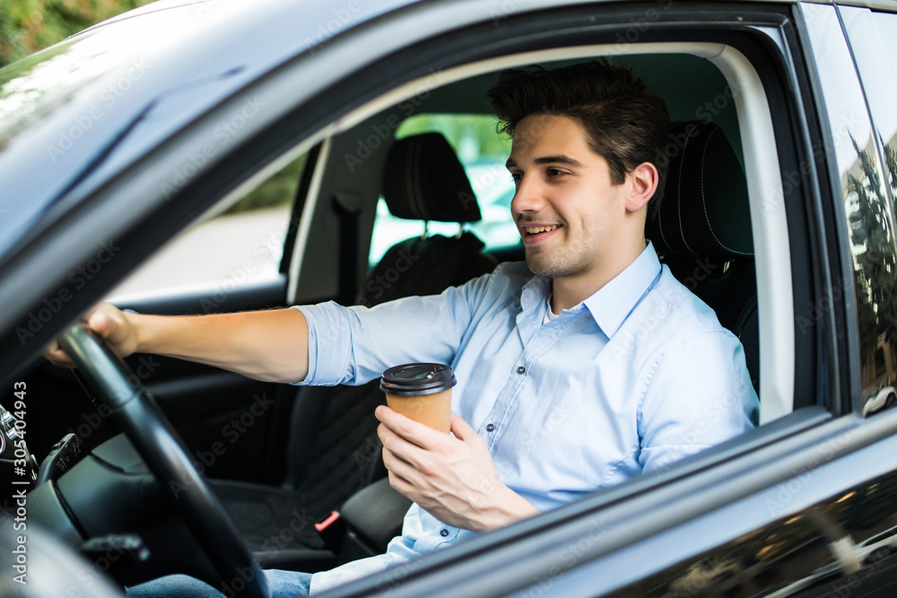 Handsome young man driving a car and holding paper cup of coffee