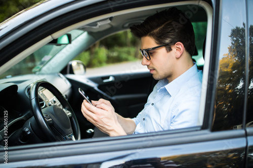 Handsome businessman sending a text message in his car