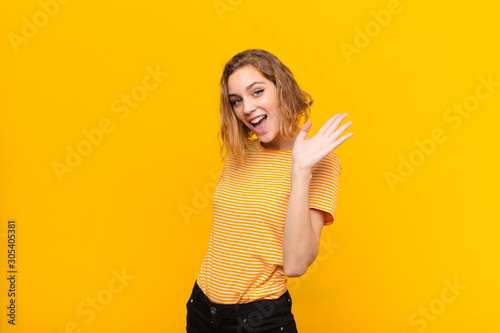 Cuadro en lienzo young blonde woman smiling happily and cheerfully, waving hand, welcoming and gr