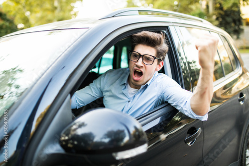 Angry young man clenching his fist, sitting in new car and shouting