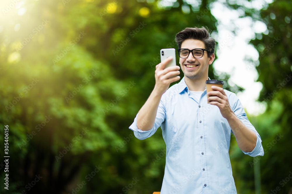 Young man wearing earpods holding and talking on smartphone while sitting in city cafe outdoors Young man wearing earpods holding and talking on smartphone while sitting in city cafe outdoors