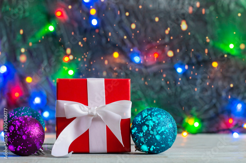 Red gift box with Christmas decorations on bokeh background and garland lights.