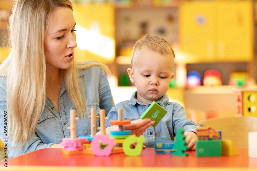 Nursery baby and carer play at table in kindergarten Nursery baby and carer play at table in kindergarten
