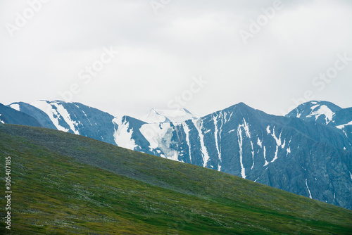 Fototapeta Atmospheric alpine landscape with green mountainside and big mountain ridge with glacier
