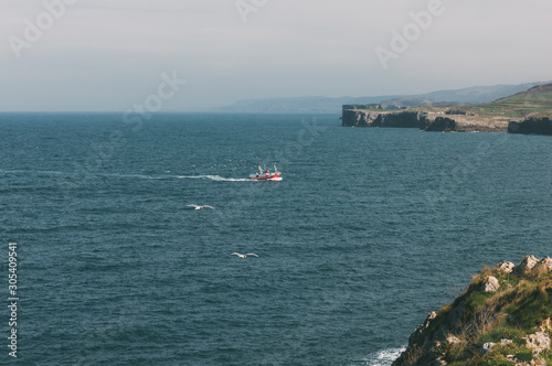 Fishing boat sailing in front of the cliffs of Llanes in Asturias