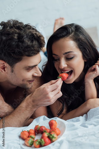 handsome man feeding attractive girlfriend with strawberry