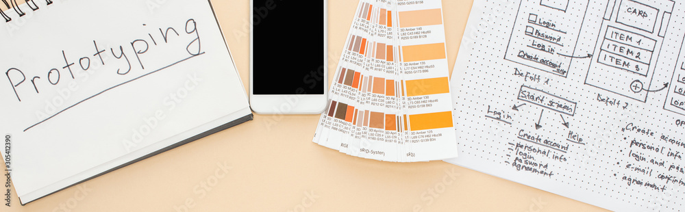 top view of smartphone near website design template, color palette and notebook with prototyping lettering on beige background, panoramic shot top view of smartphone near website design template, color palette and notebook with prototyping lettering on beige background, panoramic shot