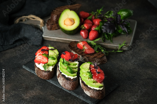 Toast or sandwich with avocado, cheese, strawberries, herbs and seeds on a dark background. An idea for bruschetta or for a healthy snack. Healthy vegan breakfast.