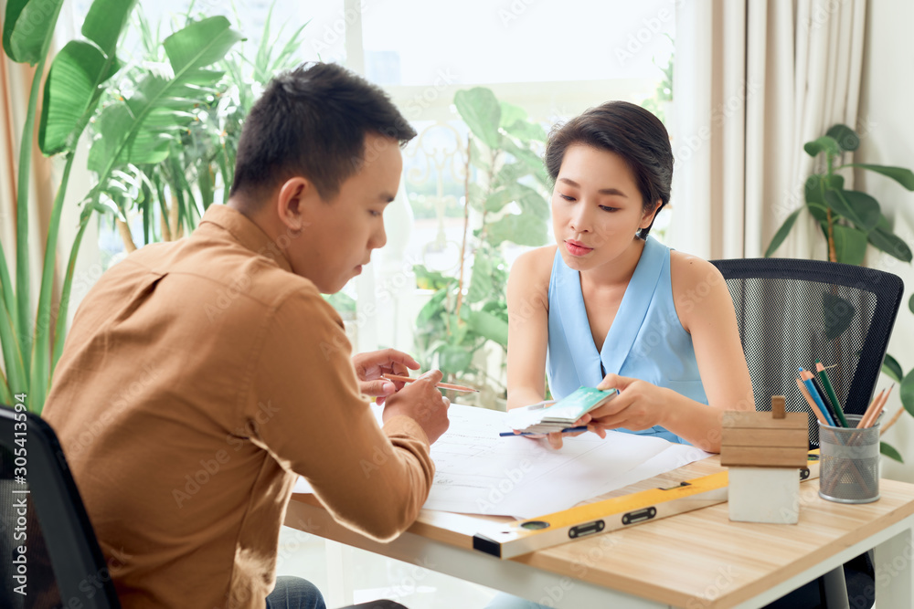Finding solution together. Confident young man and woman looking at blueprint together while both standing in office Finding solution together. Confident young man and woman looking at blueprint together while both standing in office