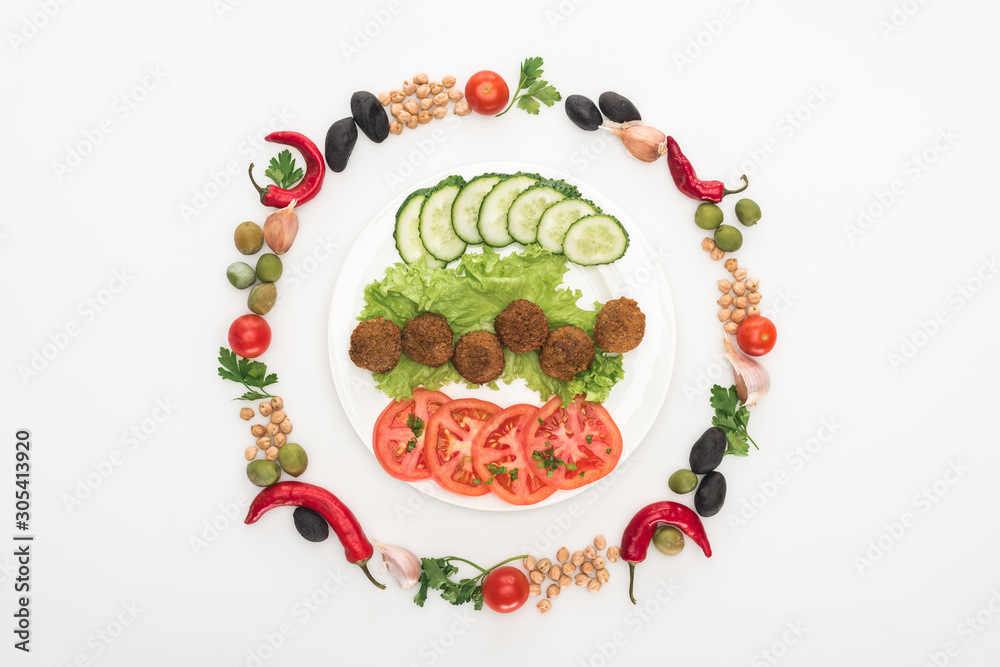 top view of vegetables arranged in round frame around falafel on plate on white background