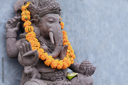 Ganesha sitting in meditating yoga pose in front of hindu temple. Decorated for religious festival by orange flowers garland, ceremonial offering. Balinese travel background. Bali island art, culture. photo