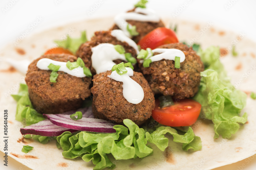 close up view of fresh falafel balls on pita with vegetables and sauce on white background