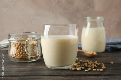 Glass of soy milk, soybeans seeds on spoon, napkin on wooden background, space for text