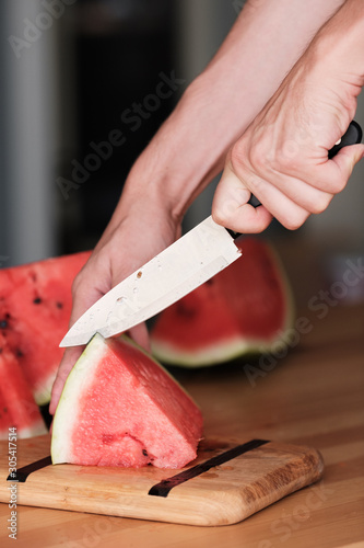 Hands chop watermelon with a knife on a bamboo cutting board