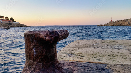 Old steel marine mooring bollard at pier at sunset