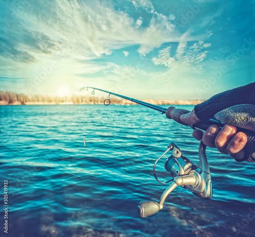 hand with spinning and reel on the summer lake