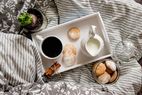 A beautiful white wooden tray with coffee, cookies and cream in a jug, on a gray background. breakfast concept in bed.