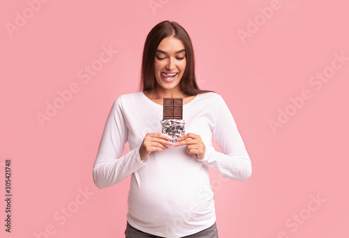 Pregnant Girl Holding Chocolate Standing Over Pink Background, Studio Shot