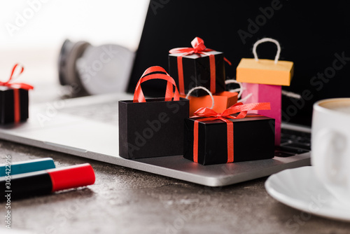 selective focus of shopping bags near laptop, cup and marker pens on white, e-commerce concept photo