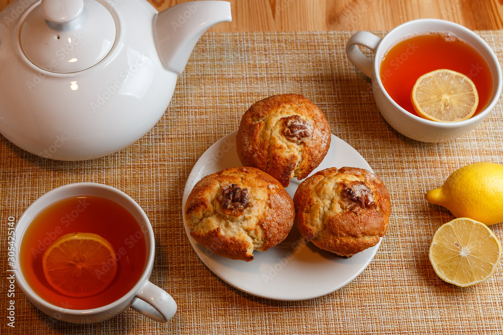 teapot is white and two white cups of tea with lemon and muffins teapot is white and two white cups of tea with lemon and muffins