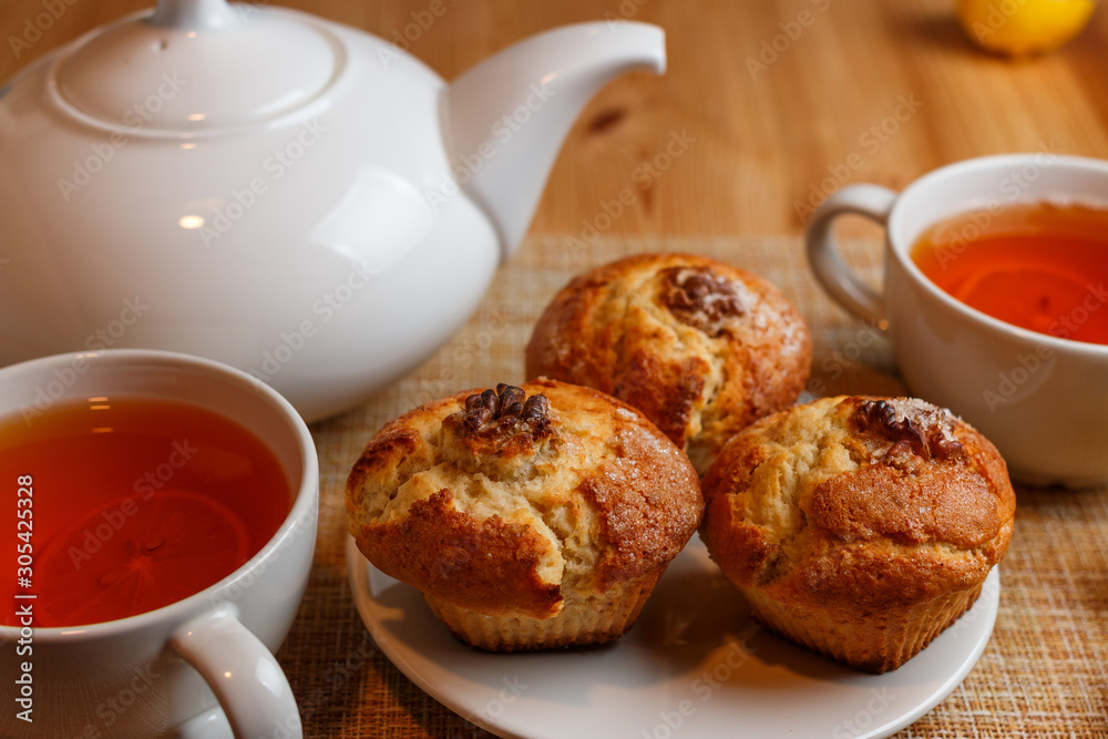 teapot is white and two white cups of tea with lemon and muffins teapot is white and two white cups of tea with lemon and muffins