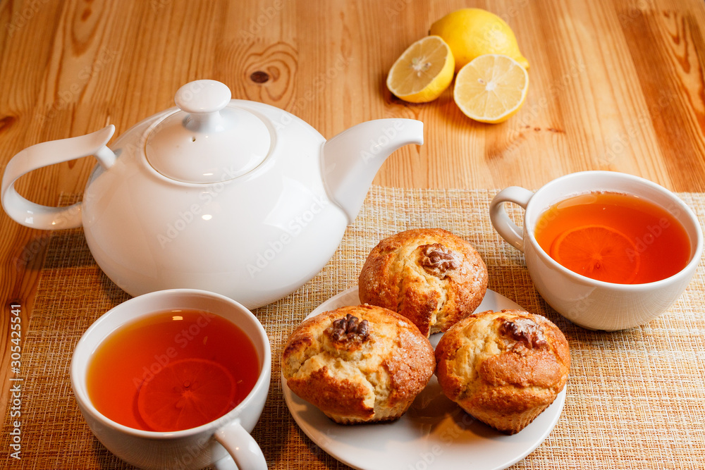 teapot is white and two white cups of tea with lemon and muffins teapot is white and two white cups of tea with lemon and muffins