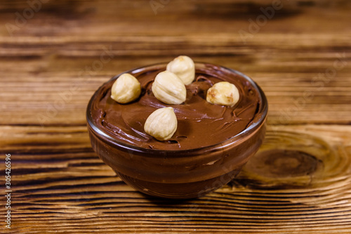 Glass bowl with chocolate spread and hazelnuts on a wooden table