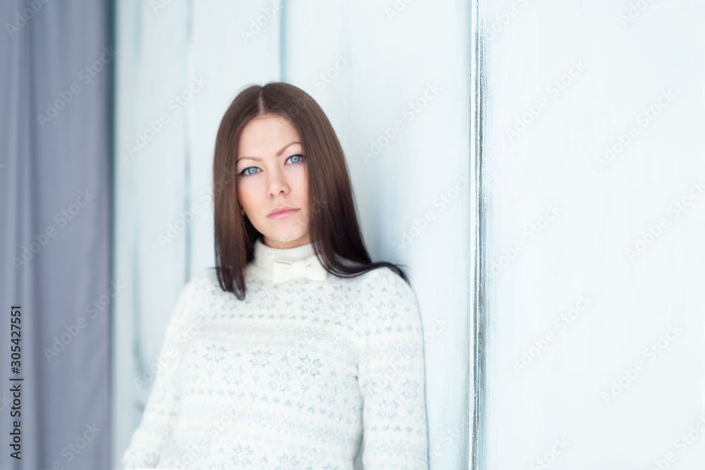 portrait of a fashionable young blue-eyed brunette in a light knitted sweater and blue jeans. portrait of a fashionable young blue-eyed brunette in a light knitted sweater and blue jeans.