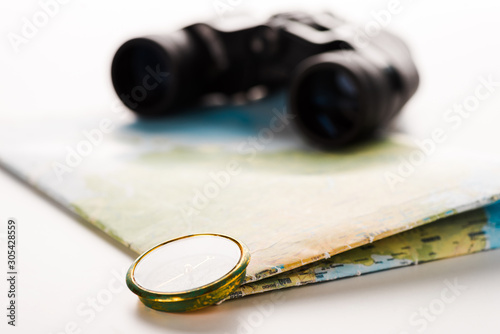 selective focus of golden compass near map and binoculars on white