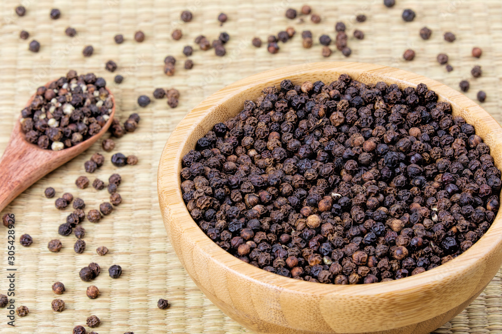 Bowl full of black peppercorns on a bamboo background Bowl full of black peppercorns on a bamboo background