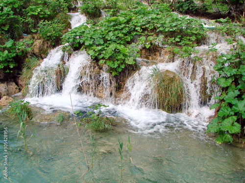 Top view of falling water into a crystal clear lake on a mountain slope richly covered with tall grass.