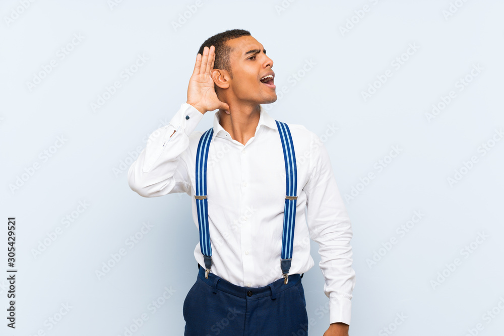 Young handsome brunette man with suspenders over isolated background listening something Young handsome brunette man with suspenders over isolated background listening something