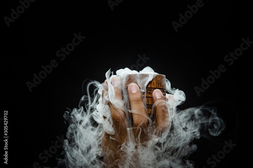 Hand smoke from dry ice in a bowl, black background.