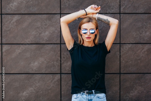 Fotografie, Obraz Girl wearing black t-shirt, glasses and leather jacket posing against street , urban clothing style